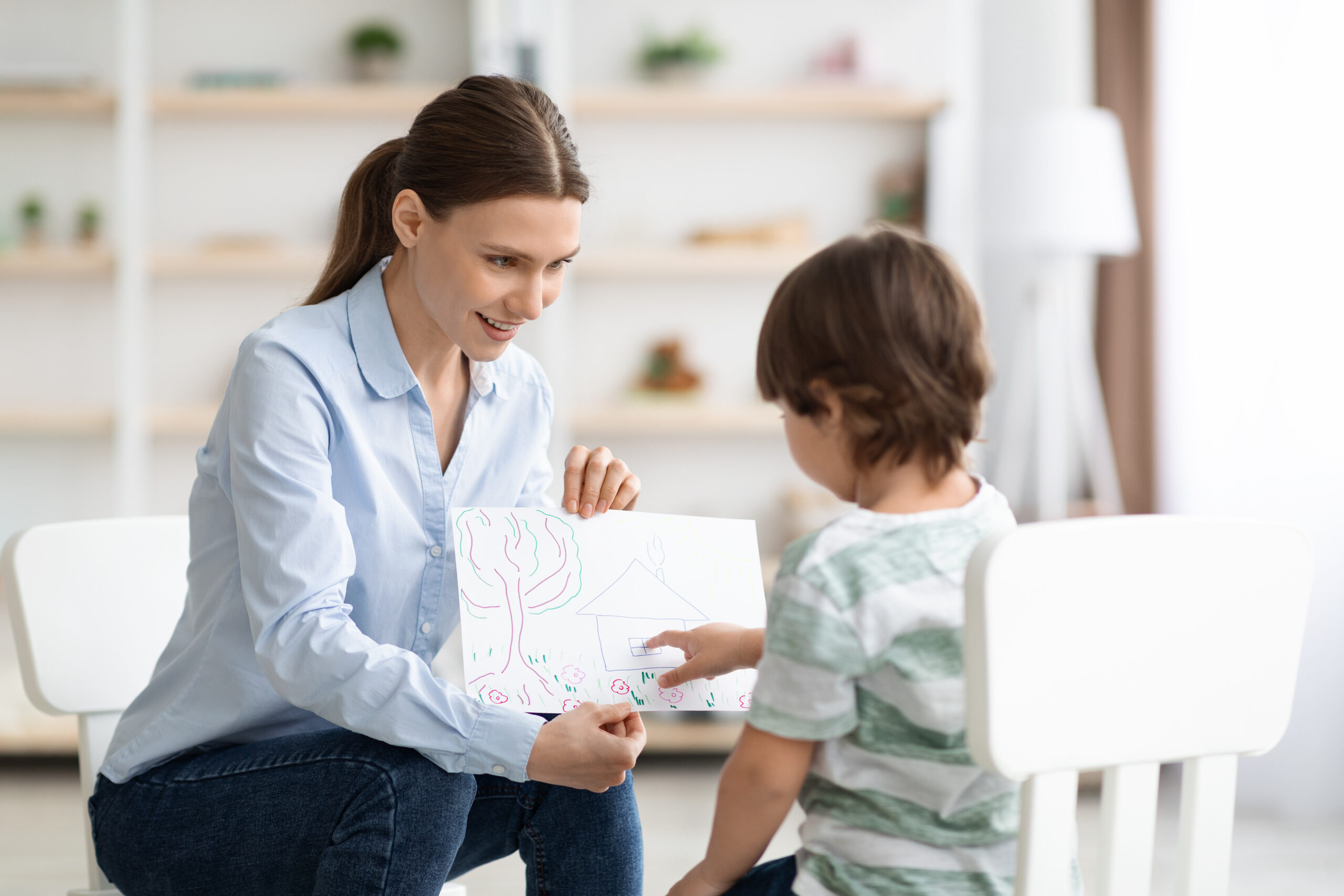 Little boy describing picture to professional woman psychologist, doctor evaluating mental health of young patient at office