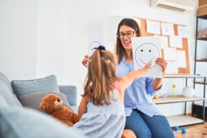 Young therapist woman speaking and treating child, counselor and behaviour correction at pedagogue payroom showing happy and sad faces